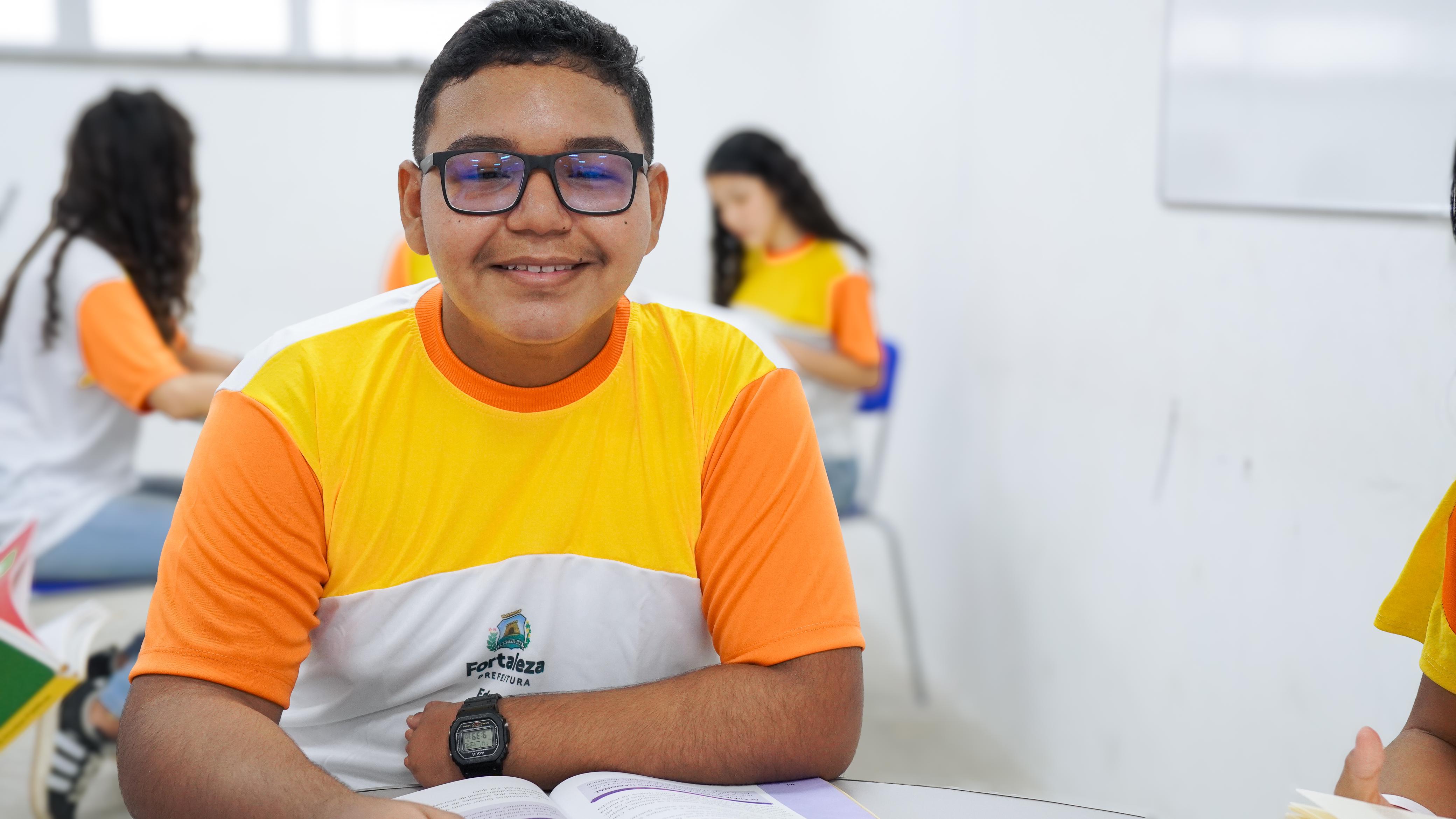 estudante fardado posa para a foto; ele é moreno e usa óculos